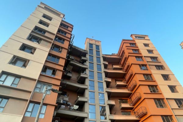 Low-angle view of Infinity Heights' modern orange and beige facade against a clear blue sky.