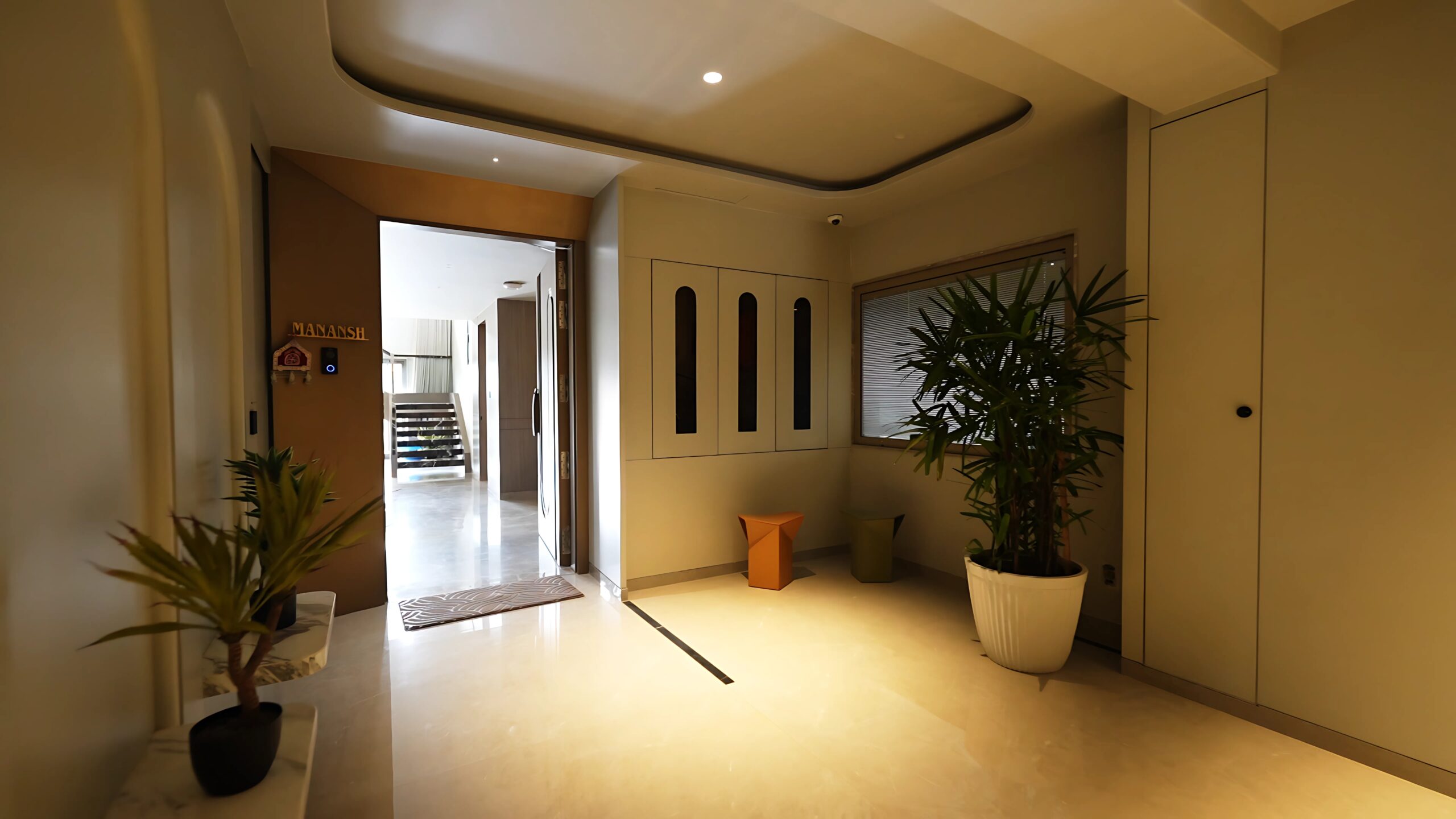 This stunning entrance showcases the epitome of a luxury villa interior, perfectly exemplifying the premium amenities found in upscale residential spaces. The sophisticated design features polished marble flooring with elegant inlays, creating an opulent atmosphere typical of a high-end apartment complex. The spacious foyer includes contemporary ceiling design with recessed lighting, highlighting the premium amenities that define luxury living. The entrance area displays modern architectural elements including decorative wall panels, strategically placed indoor plants, and refined storage solutions. The warm lighting creates an inviting ambiance, while the open-plan layout connects seamlessly to other living areas, demonstrating the spacious design characteristic of a 3 BHK flat in Guwahati. This interior exemplifies the quality and attention to detail expected in a luxury flat, featuring premium finishes, thoughtful design elements, and sophisticated aesthetics that appeal to discerning homeowners seeking upscale residential living in modern apartment complexes.