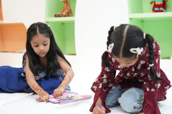 Two young girls concentrate on drawing in the kids' activity zone during the 'Parivaar Ke Sitaare' event at Infinity Heights. A wonderful amenity for families considering a 3bhk apartment in guwahati or our other flats for sale.