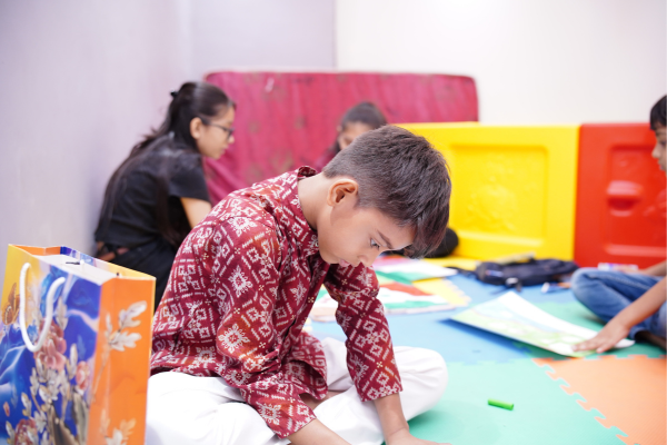 A young boy in a festive kurta concentrates on an art project while sitting on a colorful mat. This was part of a dedicated children's activity area at the Infinity Heights event.