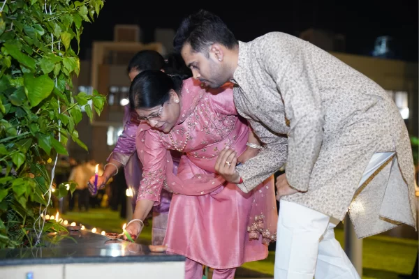 A family dressed in traditional attire bends down to light diyas together. This captures a warm, intergenerational moment at the Infinity Heights community event.