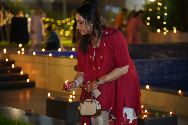 A woman with henna-adorned hands carefully lights a traditional diya by a water feature. She is participating in the beautiful lamp-lighting ceremony at Infinity Heights.