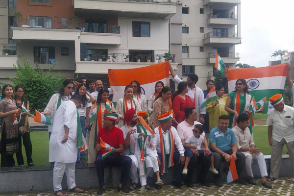 A joyful community of residents at Infinity Heights gathers for a group picture, holding large and small Indian flags to commemorate a patriotic celebration outdoors.