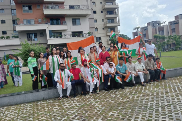 A joyful community of residents at Infinity Heights gathers for a group picture, holding large and small Indian flags to commemorate a patriotic celebration outdoors.