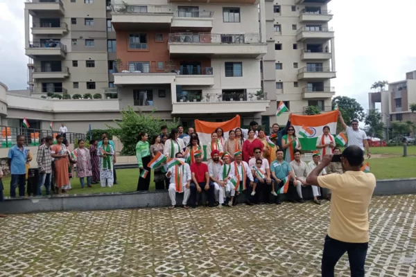 Residents of Infinity Heights, including men, women, and children, pose for a large group photo while holding Indian flags and wearing tricolor sashes, celebrating a national event.