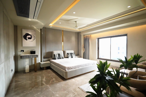 A spacious and elegantly designed master bedroom interior inside the premium 4bhk flats in guwahati at Infinity Heights, featuring polished marble flooring, a modern plush bed with a custom paneled headboard, warm cove lighting, and a large sliding window that fills the luxury room with natural light.