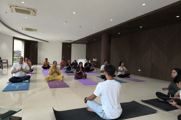 Residents at Infinity Heights, a luxury apartment in Guwahati, participate in a group yoga session inside a modern clubhouse hall with large wood pillars.