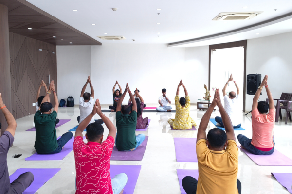 Community wellness yoga session in a bright, modern indoor hall at Infinity Heights, a premium apartment in Guwahati, featuring residents doing breathing exercises.