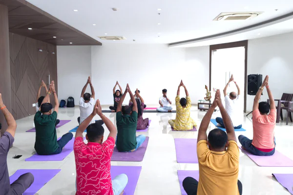 Community wellness yoga session in a bright, modern indoor hall at Infinity Heights, a premium apartment in Guwahati, featuring residents doing breathing exercises.
