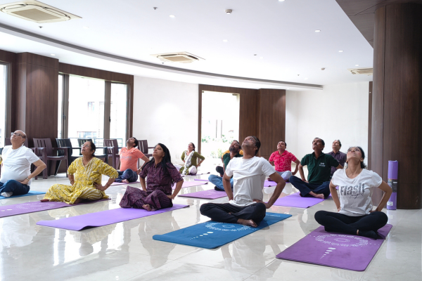 Group standing stretch session during International Yoga Day inside the bright community hall at Infinity Heights apartment in Guwahati.