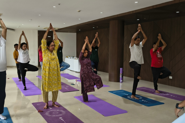 Back view of rows of residents holding a seated overhead prayer pose in the polished community hall at Infinity Heights apartment in Guwahati.