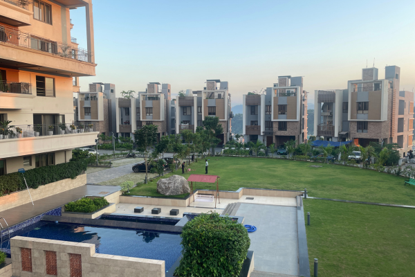 Panoramic view of a luxury residential community featuring modern villas, manicured green lawns, and a swimming pool at an assisted living facility in Kolkata.