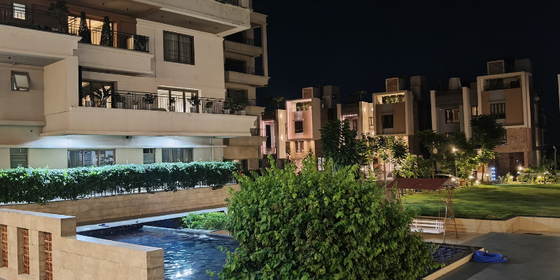 Premium modern residential enclave at night featuring upscale duplex villas, multi-story apartment balconies, an outdoor swimming pool, and illuminated landscaped courtyard gardens.