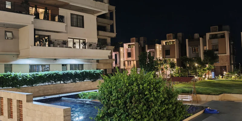 Premium modern residential enclave at night featuring upscale duplex villas, multi-story apartment balconies, an outdoor swimming pool, and illuminated landscaped courtyard gardens.