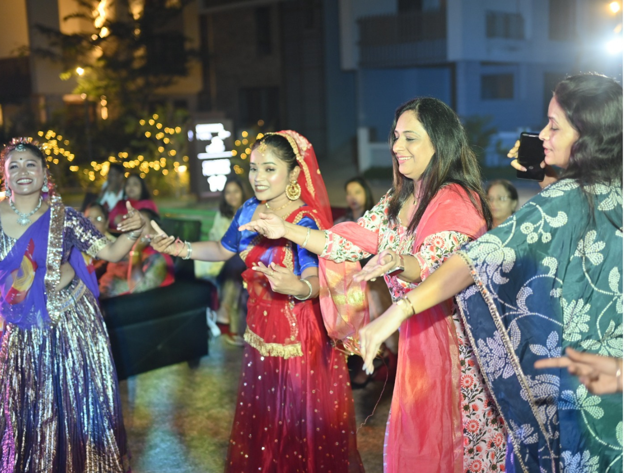 Women happily dancing and celebrating Holi in colorful traditional attire at the Infinity Heights apartment in Guwahati.