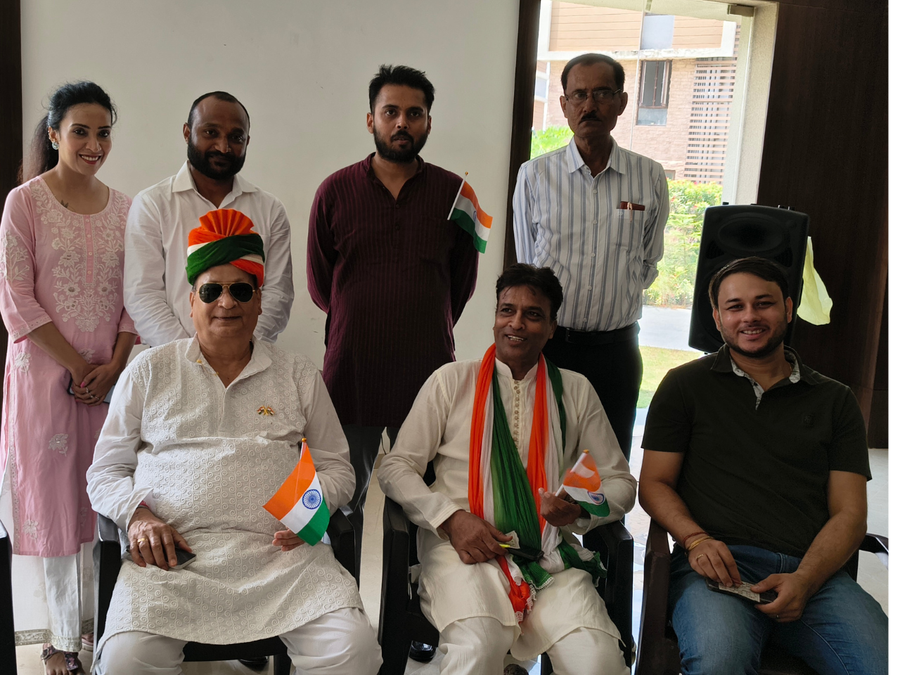 A group of residents, including a man in a tricolor turban, smiling and holding Indian flags indoors at Infinity Heights.