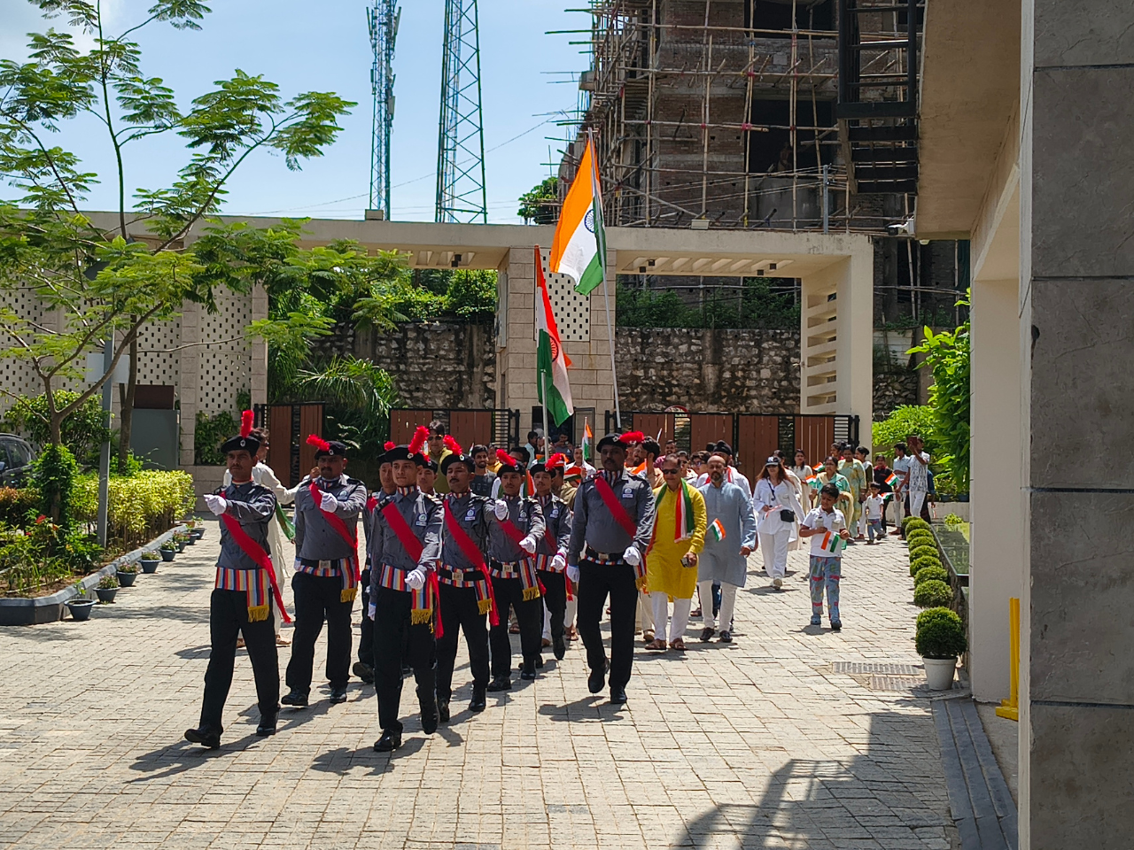 A vibrant procession of security guards and residents, including children, marching with Indian flags near the entrance of Infinity Heights.