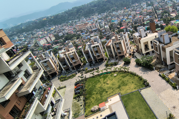 High-angle aerial view of modern residential buildings surrounding a central green lawn with a sprawling city skyline and hills in the background.