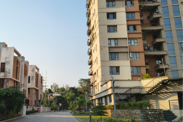 Exterior view of a multi-storey residential building and adjacent townhouses set along a paved pathway in a modern housing complex.