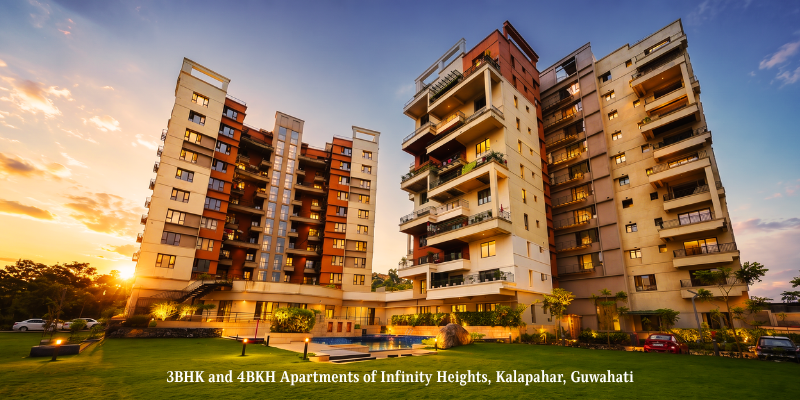 Modern multi-storey residential towers at Infinity Heights in Kalapahar, Guwahati, featuring 3BHK and 4BHK apartments, a swimming pool, landscaped lawn, and warm dusk lighting.