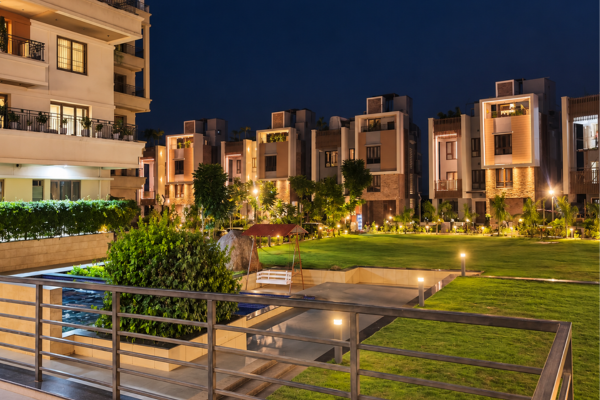 Illuminated residential buildings and villas surrounding a central landscaped lawn and garden, featuring luxury flats in guwahati at Infinity Heights.
