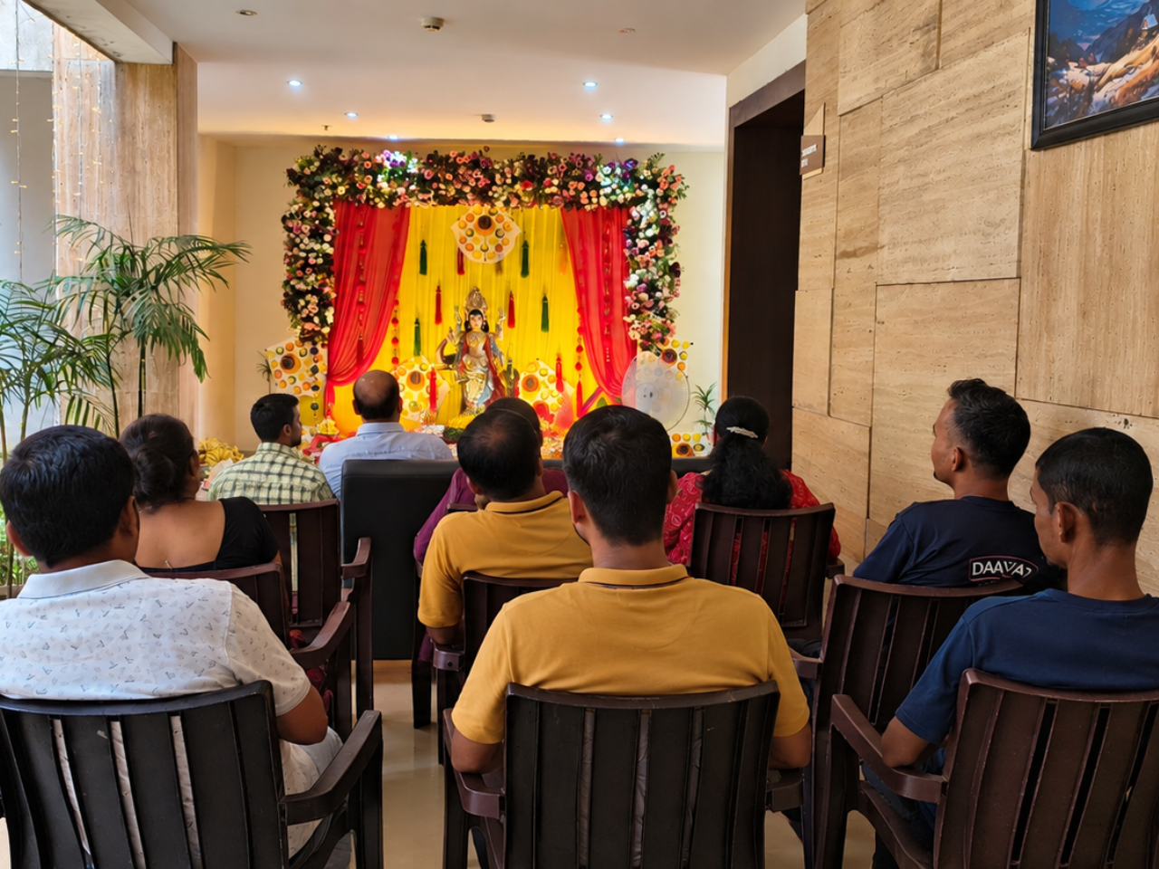 Devotees seated in rows facing a brightly decorated Vishwakarma Puja altar during a religious gathering.