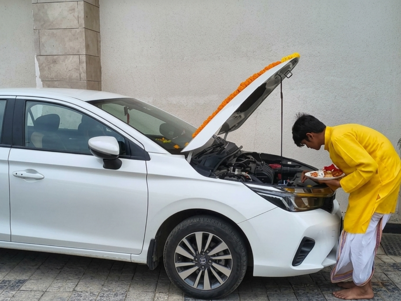 Man performing a puja ritual for a decorated new white car.
