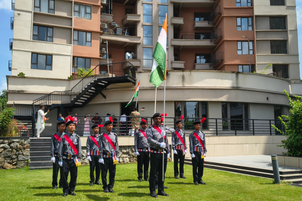 Security guards standing in formation on a green lawn holding the Indian national flag during Independence Day celebrations at Infinity Heights.