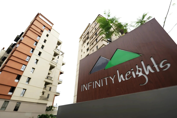 A wooden entrance sign displaying the "INFINITY heights" logo with mountain icons, framed by modern multi-storey residential towers at Infinity Heights.